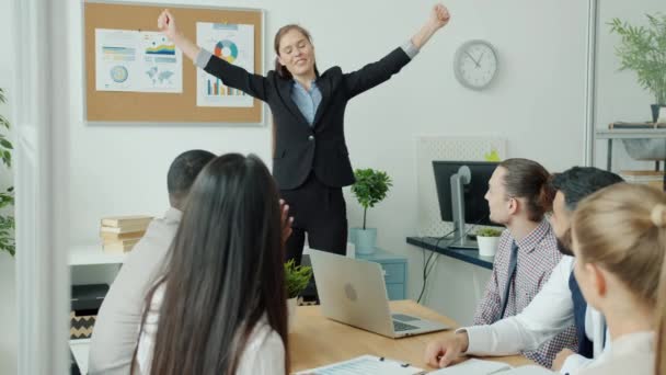 Gyönyörű öltönyös üzletasszony beszél az üzleti csapattal, aztán táncol, miközben a kollégák tapsolnak. — Stock videók