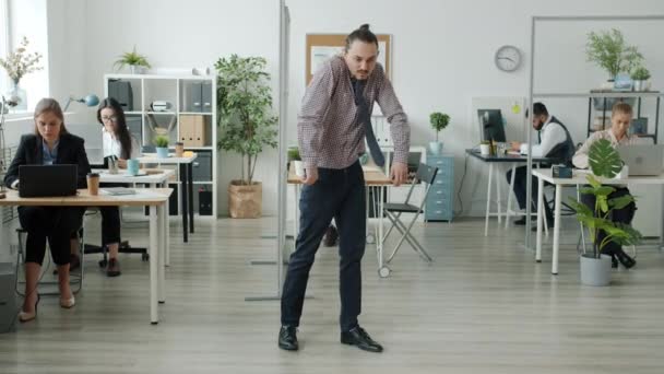 Portret zabawnego mężczyzny tańczącego w biurze podczas gdy biznesmeni pracują w tle — Wideo stockowe