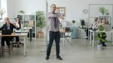 Yaratıcı adam ofiste modern dans ederken çalışanlar arka planda eğleniyor.