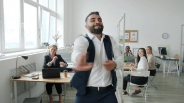 Çekici iş adamının yavaş çekim portresi ofiste dans ederken kameraya bakıyor.
