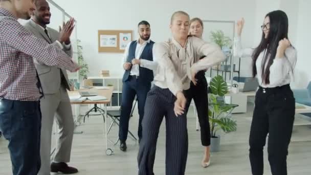 楽しさと拍手の手を持っている同僚の間で動いている企業パーティーで踊る柔軟な若い女性 — ストック動画