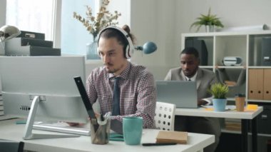 Bilgisayarda yazı yazan mutlu bir çalışan. Sonra dans ediyor. Kulaklıkla müzik dinliyor.