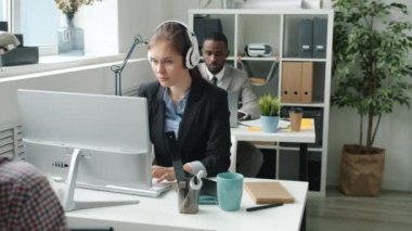 Bilgisayarla çalışan, kulaklıkla müzik dinleyen ve dans eden çekici genç bir iş kadını.