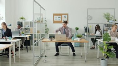 Başarılı bir ofis çalışanı dizüstü bilgisayar kullanıp dans ederken iş adamları başarıyı alkışlıyor.