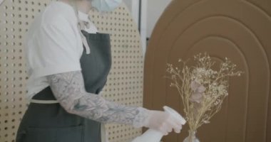 Yüz maskesi eldivenleri ve önlük takan garson, kahve masasını dezenfektan jeliyle dezenfekte ediyor.