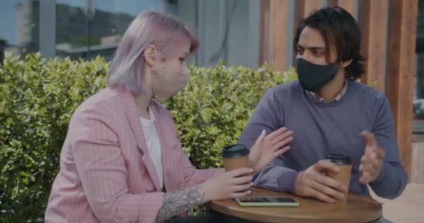 Alegre pareja de raza mixta hablando y tomando café en la cafetería al aire libre durante la epidemia de covid-19 — Vídeos de Stock
