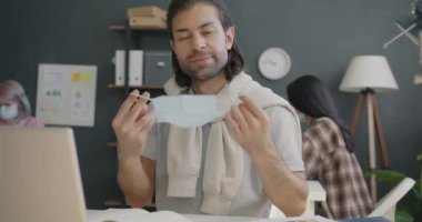 Çekici bir ofis çalışanının portresi tıbbi maske takıyor ve iş yerindeki kameraya bakıyor.