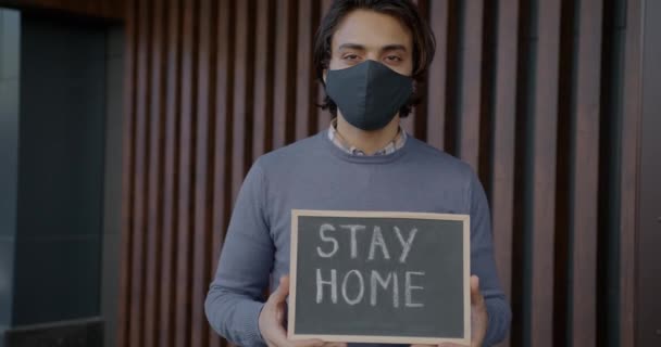 Portrait de jeune homme arabe tenant un tableau craie avec message Stay home — Video