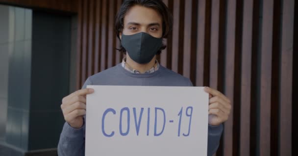 Portret zdrowego faceta z Bliskiego Wschodu trzymającego plakat Covid-19 na zewnątrz — Wideo stockowe
