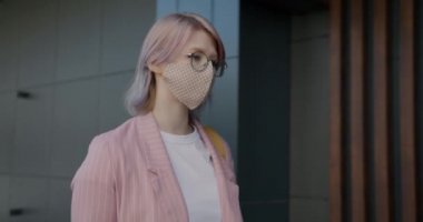 Yüzünde maske olan neşeli genç bir kadın dışarıda akıllı telefon kullanıyor.