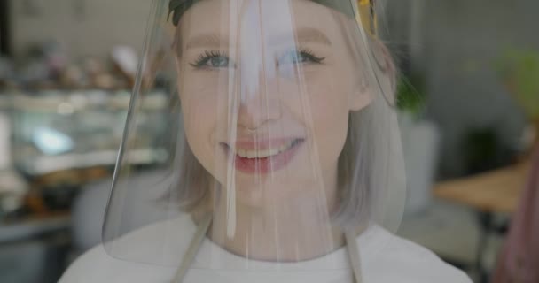 Retrato de jovem garçonete loira usando protetor facial em pé no café e olhando para a câmera — Vídeo de Stock