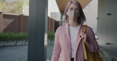 Çekici, yüz maskesi takmış genç bir kadının boş bir caddede yürüdüğü bir resim.