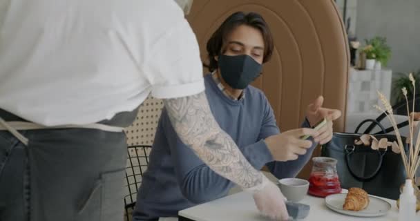 Arabe gars portant un masque et des gants payer avec smartphone dans le café profiter de la pause déjeuner — Video