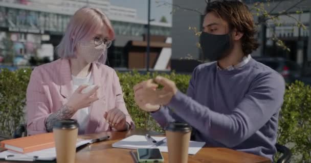 Étudiants portant des masques étudiant dans un café de rue vaporisant des mains avec un désinfectant — Video