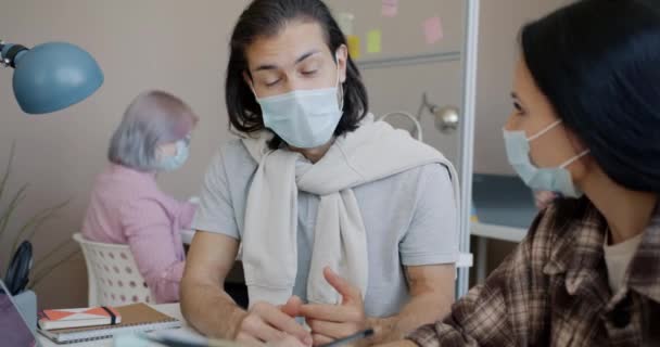 Homem de raça mista usando máscara médica trabalhando no escritório conversando com colega e usando laptop — Vídeo de Stock