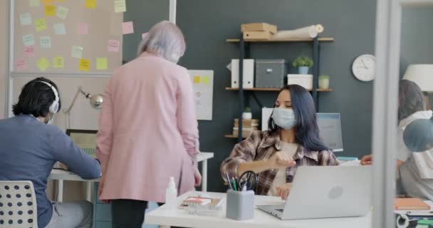 Jeune femme portant un masque facial faisant bosse du coude avec un collègue et travaillant avec un ordinateur au bureau — Video
