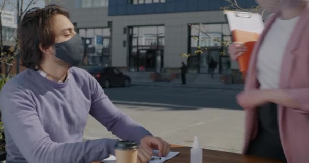 Mujer joven reunión socio de negocios en la cafetería al aire libre desinfectante manos hablando usando máscara — Vídeos de Stock