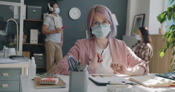 Portrait de jeune femme faisant un appel vidéo du bureau portant un masque regardant la caméra et parlant — Video