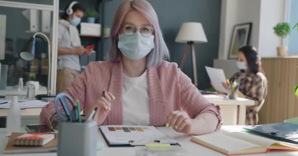 Retrato de funcionária usando máscara médica fazendo videochamada no local de trabalho — Vídeo de Stock