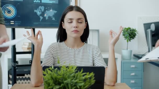 Vacker ung kvinna mediterar i ämbetet med slutna ögon medan kollegor talar och tar med papper — Stockvideo