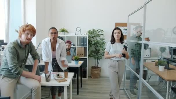 Emotionale Büroangestellte, die auf die Kamera zeigen und lachen, machen drinnen am Arbeitsplatz lustige Gesichter — Stockvideo