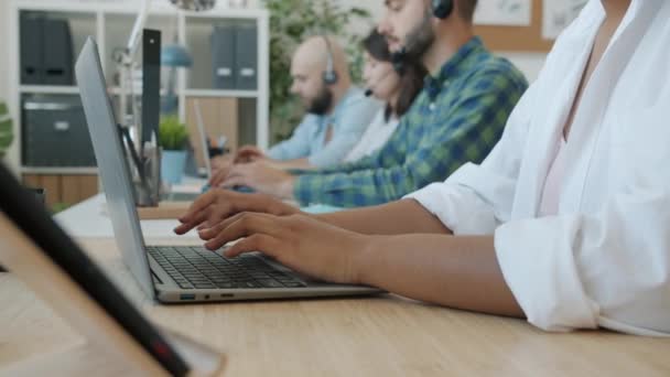 Close-up de mãos femininas digitando com laptop, enquanto as pessoas em segundo plano trabalhando no call center — Vídeo de Stock