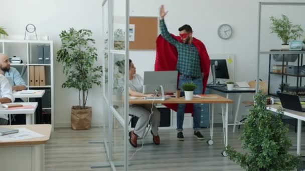 Divertido joven en traje de superhéroe corriendo en la oficina haciendo chocar los cinco con sus colegas — Vídeos de Stock