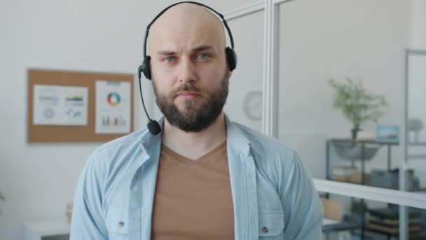 Portret spowolnionego ruchu męskiego specjalisty call center noszącego słuchawki stojące w biurze z poważną twarzą — Wideo stockowe
