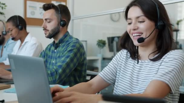 Unga dam callcenter operatör prata med kunden och ler med bärbar dator på jobbet — Stockvideo