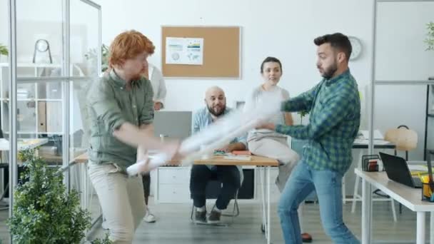 Verspielte Männer Büroangestellte kämpfen mit Papierschwertern und genießen lustige Aktivitäten bei der Arbeit — Stockvideo