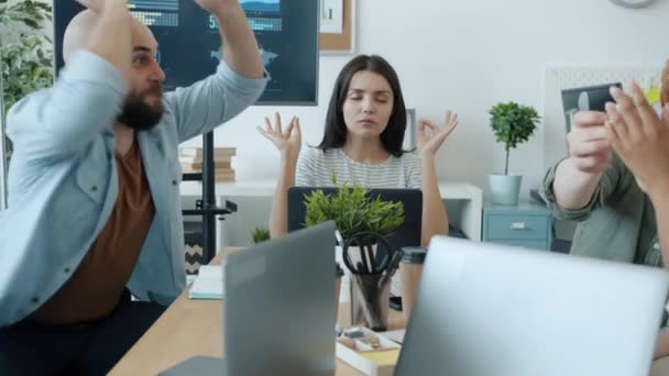 Бізнес-леді медитує в офісі, в той час як радісні колеги кидають паперові кульки розважаються — стокове відео