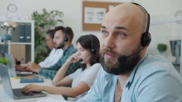Attraktiver Typ mit Headset im Gespräch mit Kunden, die im technischen Kundendienst im Büro arbeiten — Stockvideo