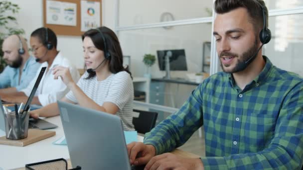 Schöner Mann Call Center Agent im Gespräch mit Client mit Laptop dann Notizen machen — Stockvideo