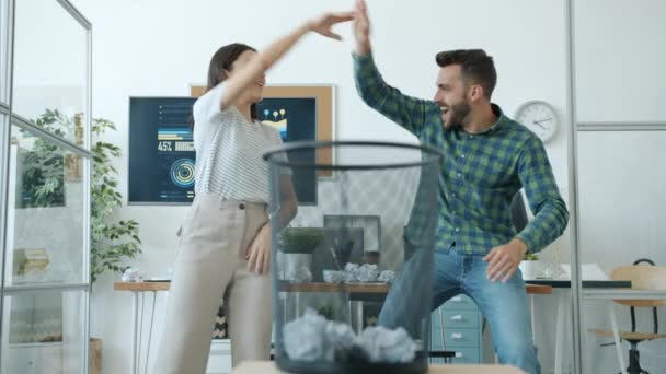 Radostný muž a žena hraje basketbal v úřadu házení papírových míčků v košíku dělá high-five smích — Stock video