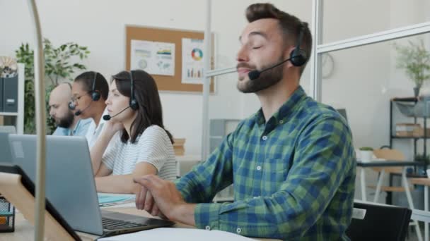 Müder Kerl, der im Callcenter arbeitet und dann den Kopf auf den Tisch legt und sich erschöpft fühlt — Stockvideo