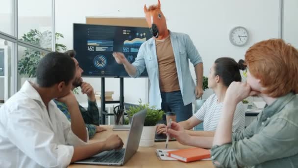 Businessman wearing horse head mask making presentation in office to group of employees — Stock Video