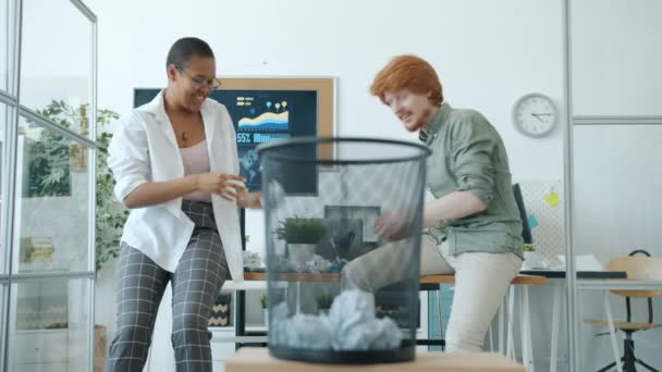 Афроамериканська дівчина і кавказький хлопець кидають паперові кульки в смітник, роблячи п'ять на роботі. — стокове відео