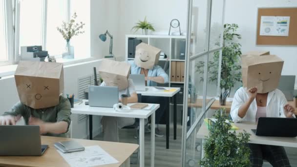 Empleados masculinos y femeninos con bolsas de papel sobre cabezas ocupadas con actividades de oficina y expresando emociones — Vídeo de stock