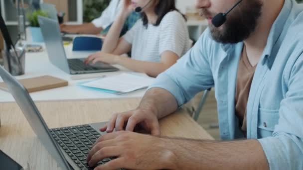 Spesialis layanan pelanggan pria berbicara dan mengetik menggunakan laptop di kantor modern — Stok Video