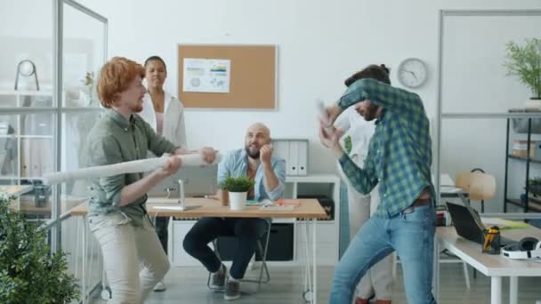 Mouvement lent des hommes d'affaires fous combattant des épées de papier tandis que des collègues acclamant dans le bureau — Video