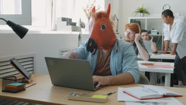 一个戴着面具，带着笔记本电脑打字的有趣男人把精力集中在办公室的商务活动上 — 图库视频影像