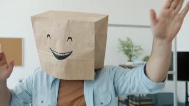 Ofiste kafasında emoji resmi olan ekmek çantası takan neşeli bir çalışanın yavaş çekim portresi.