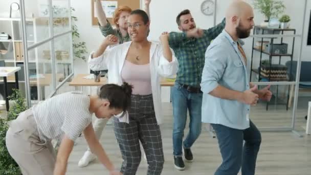 Cámara lenta de empleados alegres diversos bailes en grupo divirtiéndose en la oficina — Vídeos de Stock