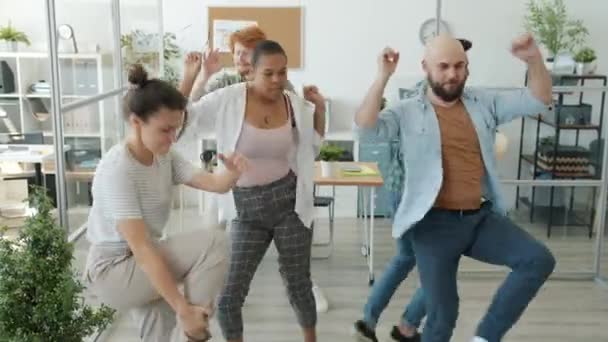 Божевільні молоді дівчата та хлопці танцюють на робочому місці роблячи смішні рухи та обличчя — стокове відео