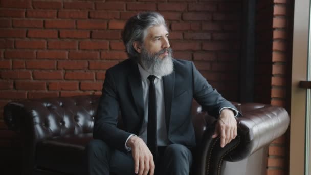 Портрет зрелого бизнесмена, сидящего на диване в мансарде — стоковое видео