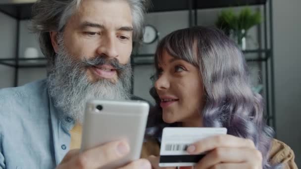 Joyful man en vrouw winkelen online betalen met creditcard en smartphone lachen binnen — Stockvideo