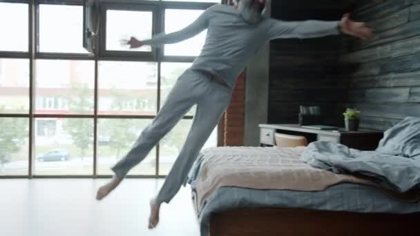 Mouvement lent de l'homme mature portant un pyjama sautant dans le lit à la maison en profitant du repos seul — Video