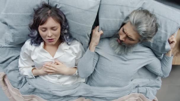 Jovem mulher roncando no sono enquanto marido irritado cobrindo a cabeça com travesseiro — Vídeo de Stock