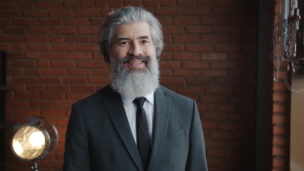 Portrét atraktivního zralého podnikatele s úsměvem při pohledu na kameru uvnitř s cihlovou zdí v pozadí — Stock video