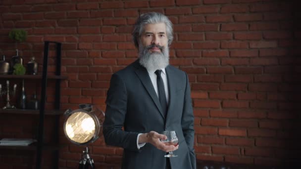 Portrét pohledného zralého podnikatele stojící v podkrovní kanceláři se sklenicí koňaku — Stock video